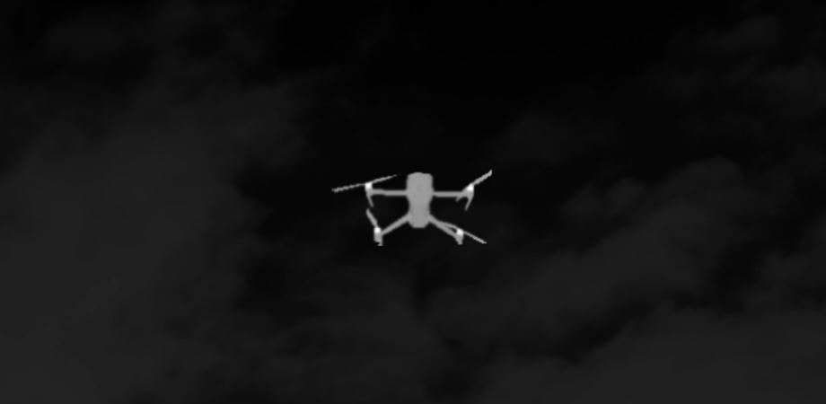 Thermal or infrared simulation of a drone in flight against a dark sky background.