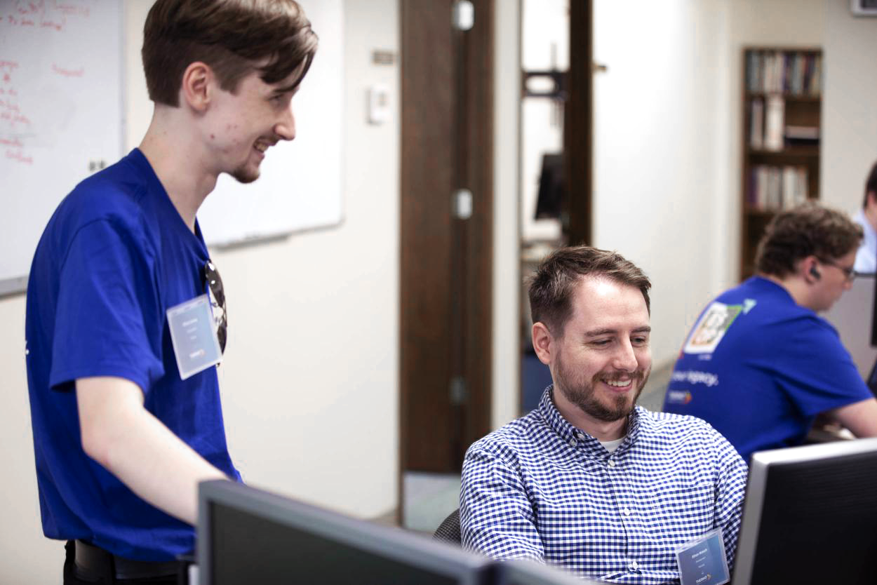Two coworkers collaborating at a desk, smiling while looking at a computer screen.
